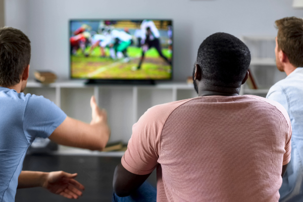 Three friends sit in front of a television watching a streaming football game.
