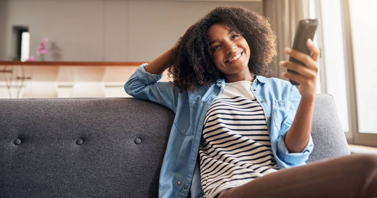 A young woman points her remote control at her smart TV and watches a streaming show. CTV completion rates now outperform other forms of viewing.