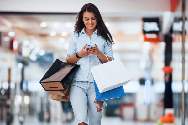A young woman browses her phone while shopping in a mall.