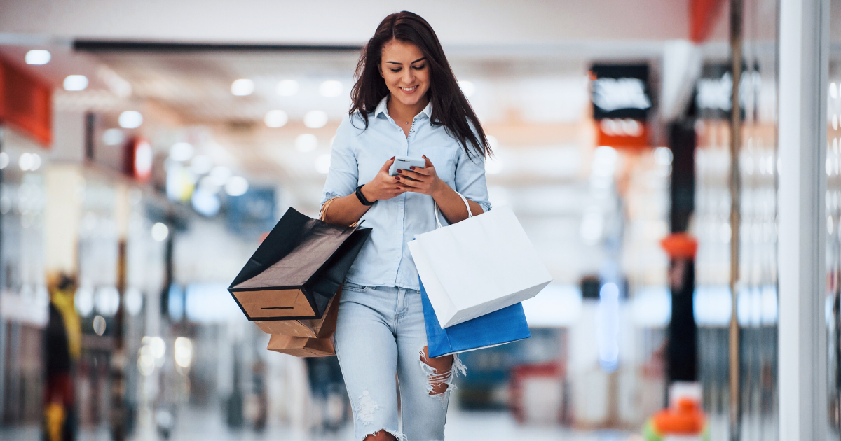 A young woman browses her phone while shopping in a mall.