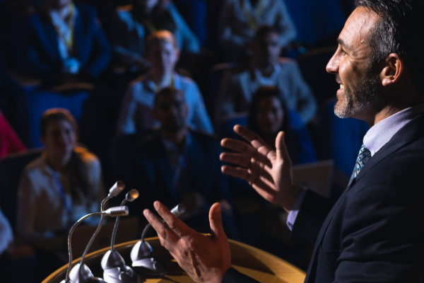 A politician stands at a podium with his hands raised while giving a speech to a crowd.