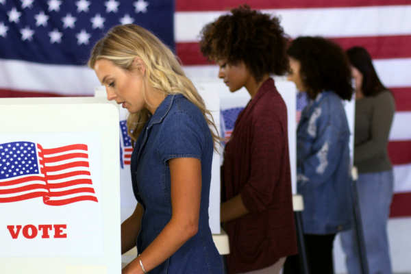 Four women motivated by FDS Political Ads are lined up to vote with an American flag in the background,