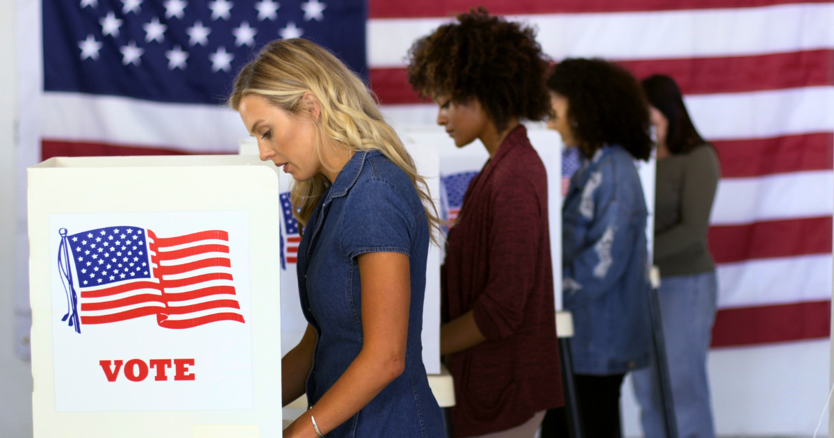 Four women motivated by FDS Political Ads are lined up to vote with an American flag in the background,