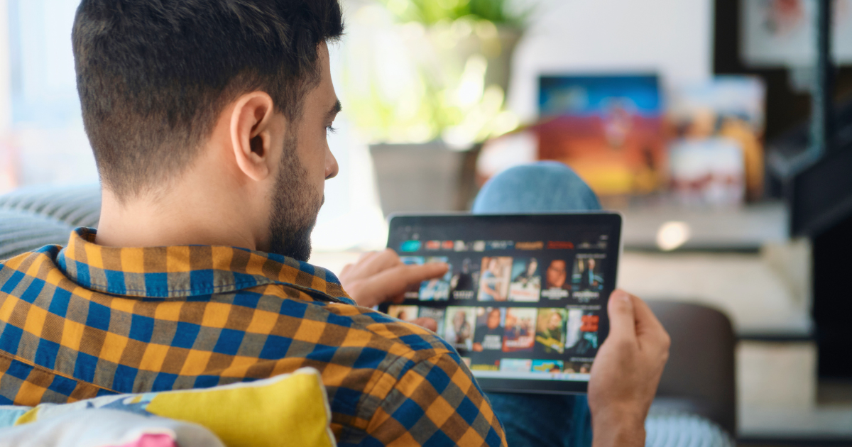 A man looks at his tablet and browses streaming shows to watch.