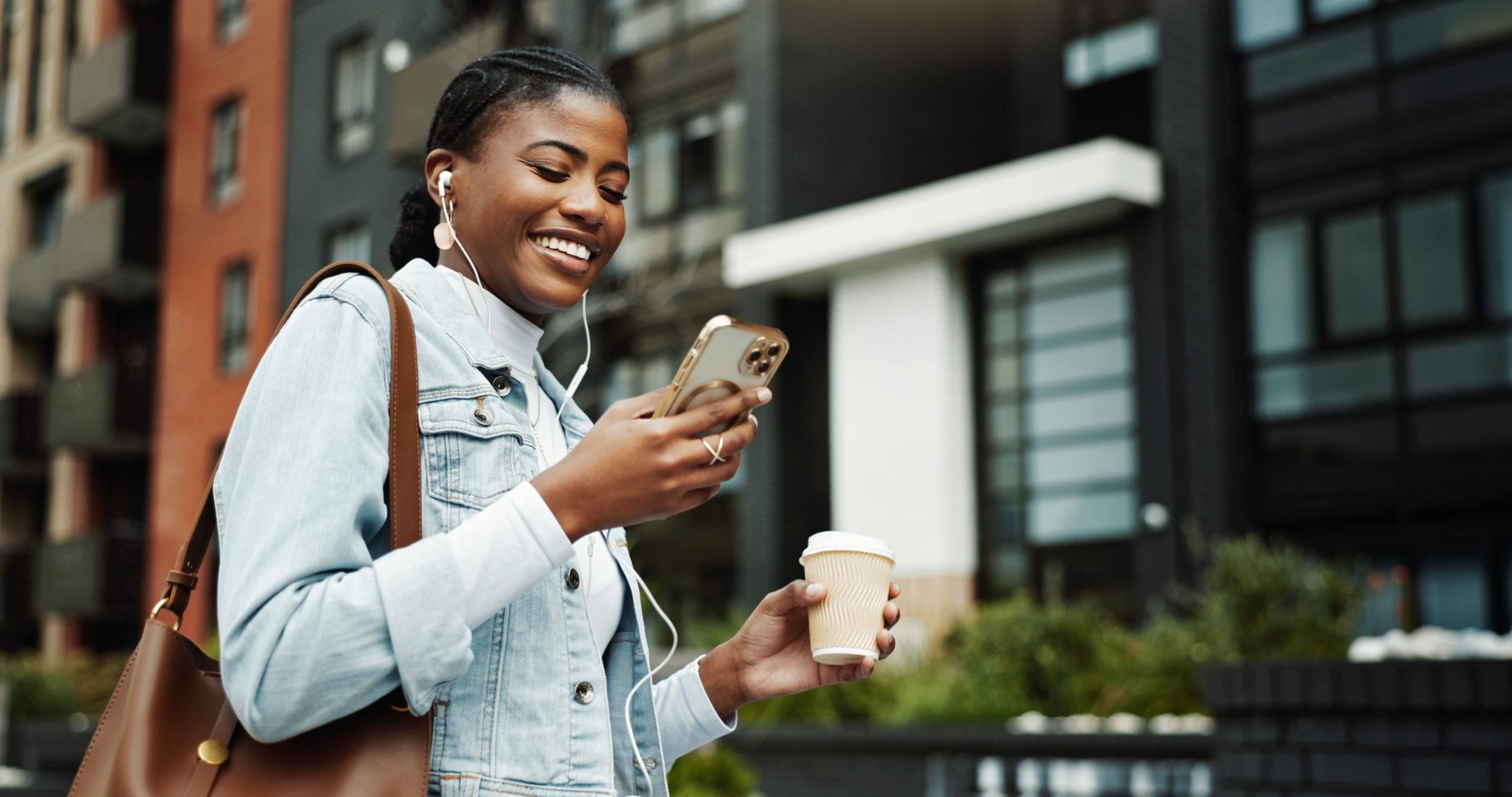 A young woman walks down the street listening to programmatic audio on a podcast while enjoying coffee.
