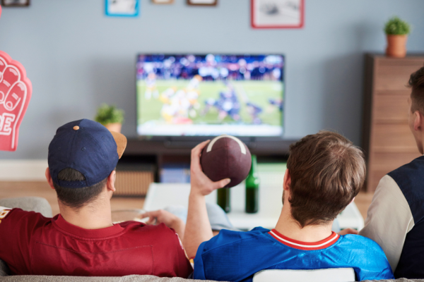 Three friends sit on a couch watch a live sporting event on streaming services.