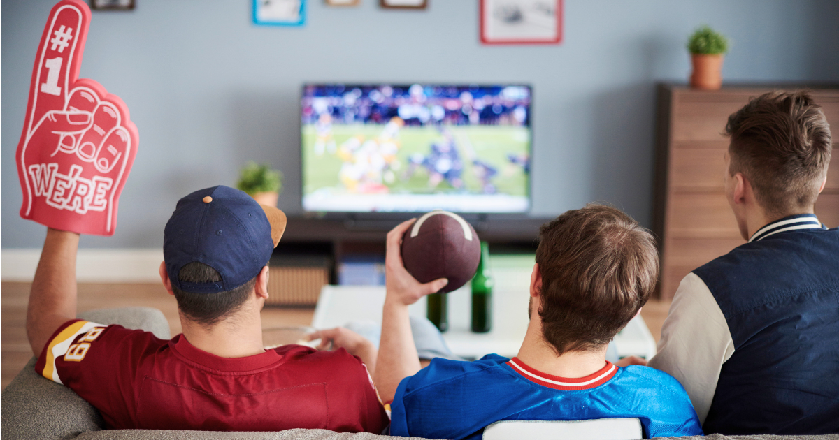 Three friends sit on a couch watch a live sporting event on streaming services.
